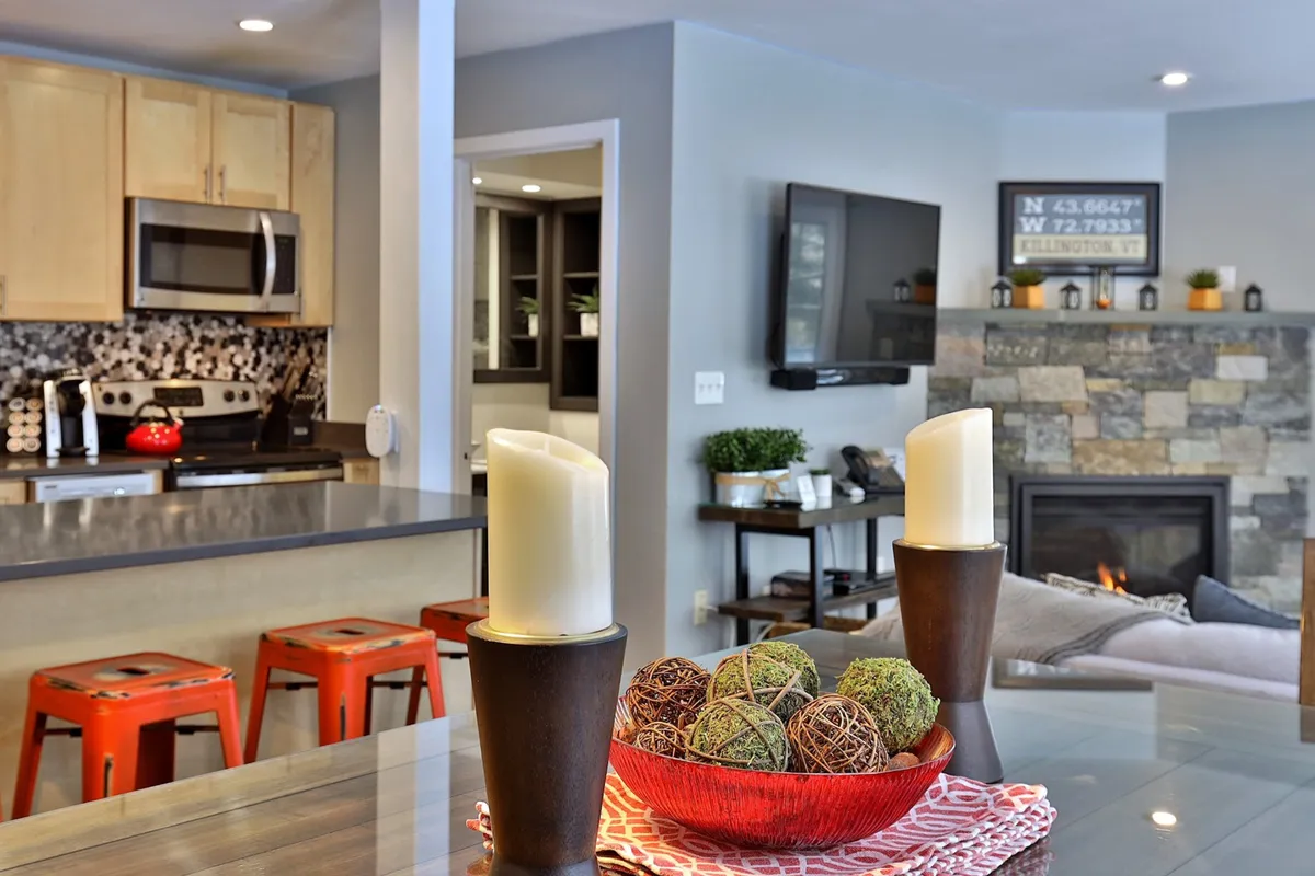 An inviting living area featuring a kitchen island with bar stools, a decorative bowl, a cozy fireplace, and a TV. The space exudes comfort and warmth, ideal for relaxing after a day of adventure or enjoying streaming entertainment. The modern yet homey design makes it suitable for family or small group gatherings in any season.