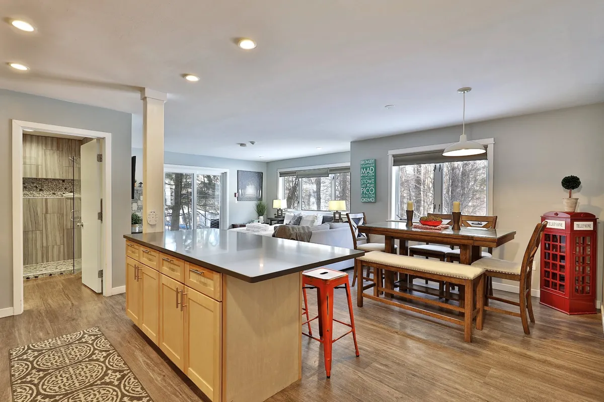 A spacious, inviting interior with a kitchen island, dining table, and a red telephone booth accent. Large windows flood the space with natural light, while the seating arrangement encourages socializing, dining, and group gatherings.