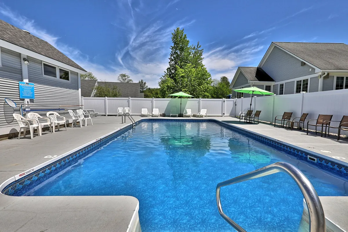 This image features a sparkling swimming pool surrounded by lounge chairs and green umbrellas, nestled among tall trees. The inviting pool area suggests a perfect summer retreat and the communal, relaxed atmosphere is evident. The lush greenery and clear pool water hint at refreshing moments in warmer months.