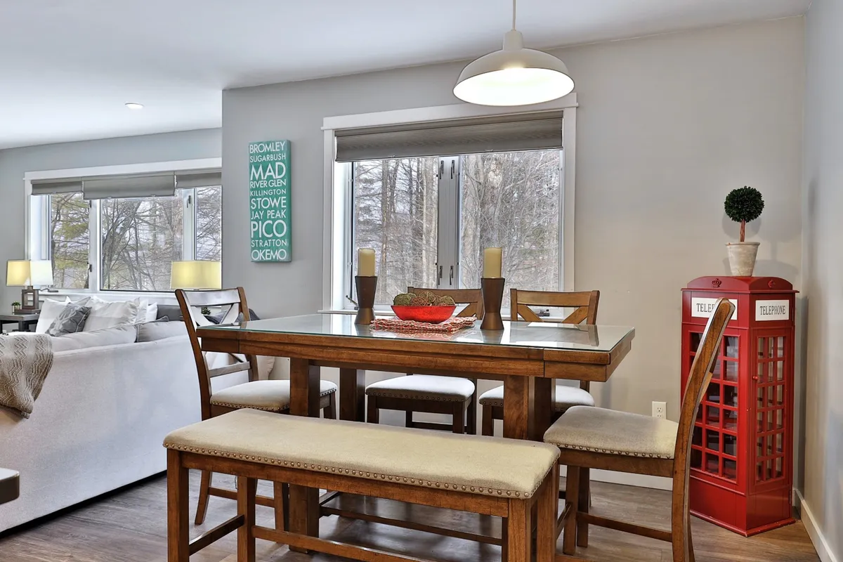 A cozy dining area anchored by a high-top table, a whimsical red telephone booth, and a decorative wall sign. The arrangement invites group meals, celebrations, and game nights in a warm, inviting setting.