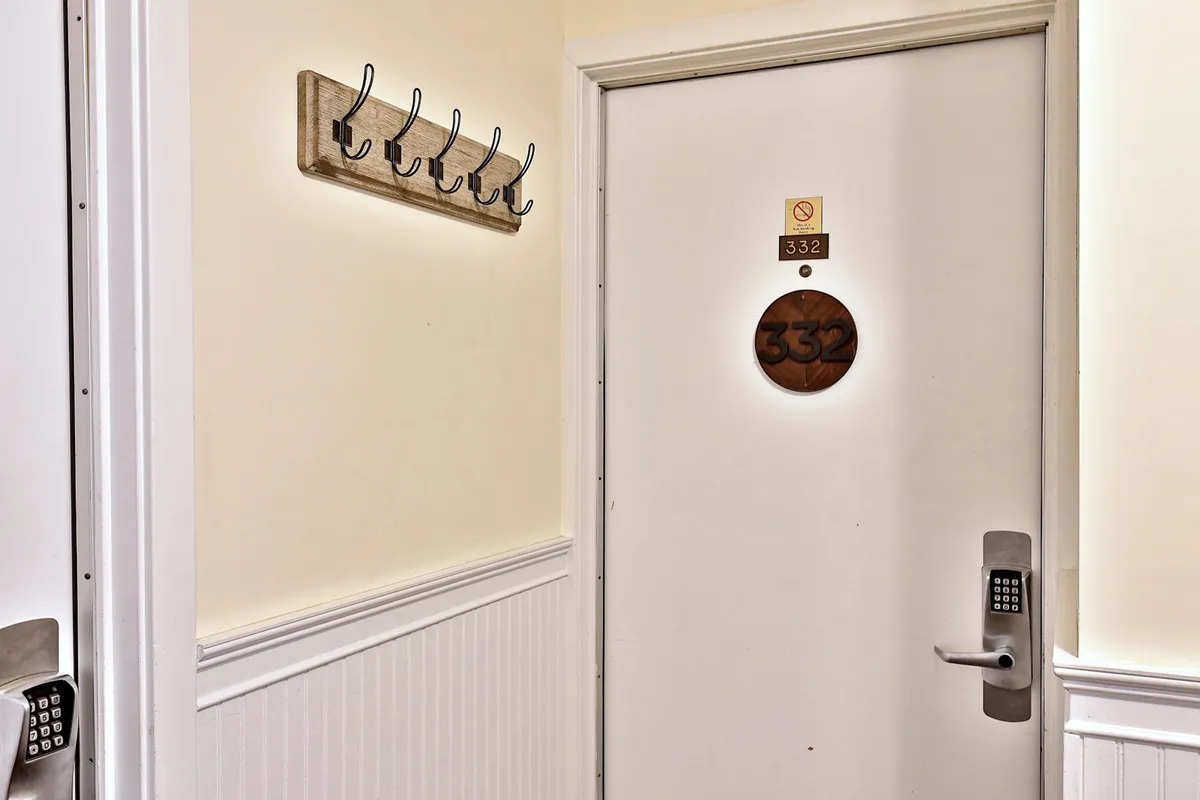 This image features a welcoming entryway with a clearly marked door number, convenient wall hooks for coats or bags, and a sturdy door handle, setting the stage for the guest's arrival and sense of independence. The area is inviting and emphasizes ease of access to one's private space.