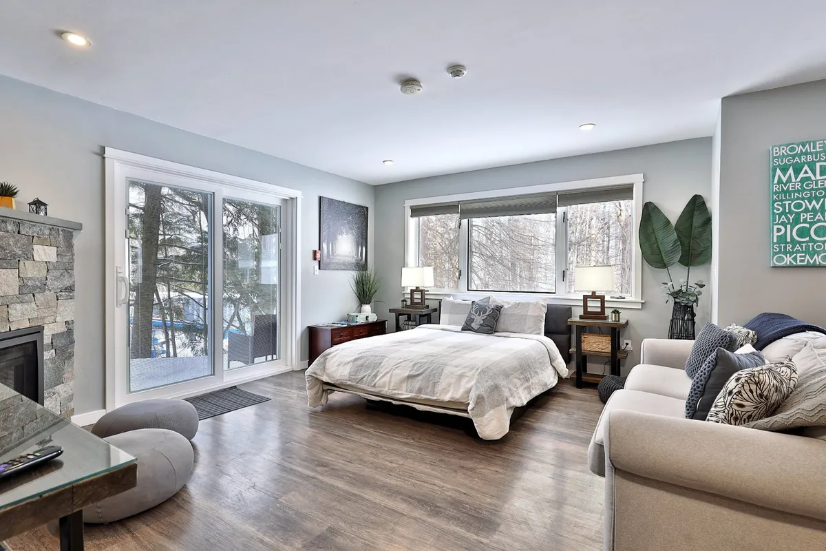 A comfortable living area featuring a plush bed, sofa, fireplace, large windows, and a decorative wall. Natural light flows in, and the fireplace and seating create a warm, communal retreat perfect for unwinding together after adventures.