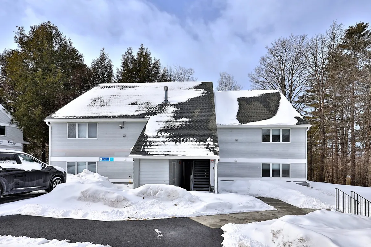 This exterior shot showcases a snow-covered building with a visible staircase entrance, surrounded by wintry trees and a driveway blanketed in snow. The serene winter landscape sets the stage for outdoor snow play and cozy returns after a day on the slopes.