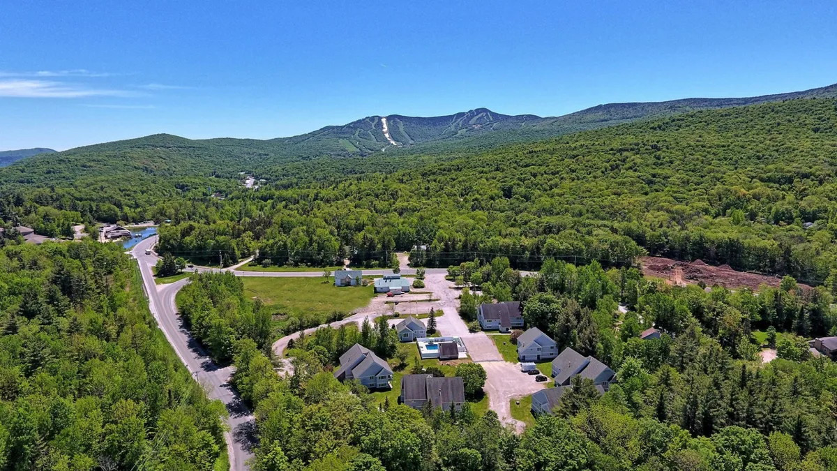 A sweeping exterior view of the Killington area, featuring a picturesque mountain range, clusters of houses, winding roadways, and lush greenery. The landscape suggests opportunities for outdoor adventures and group activities in a scenic environment.