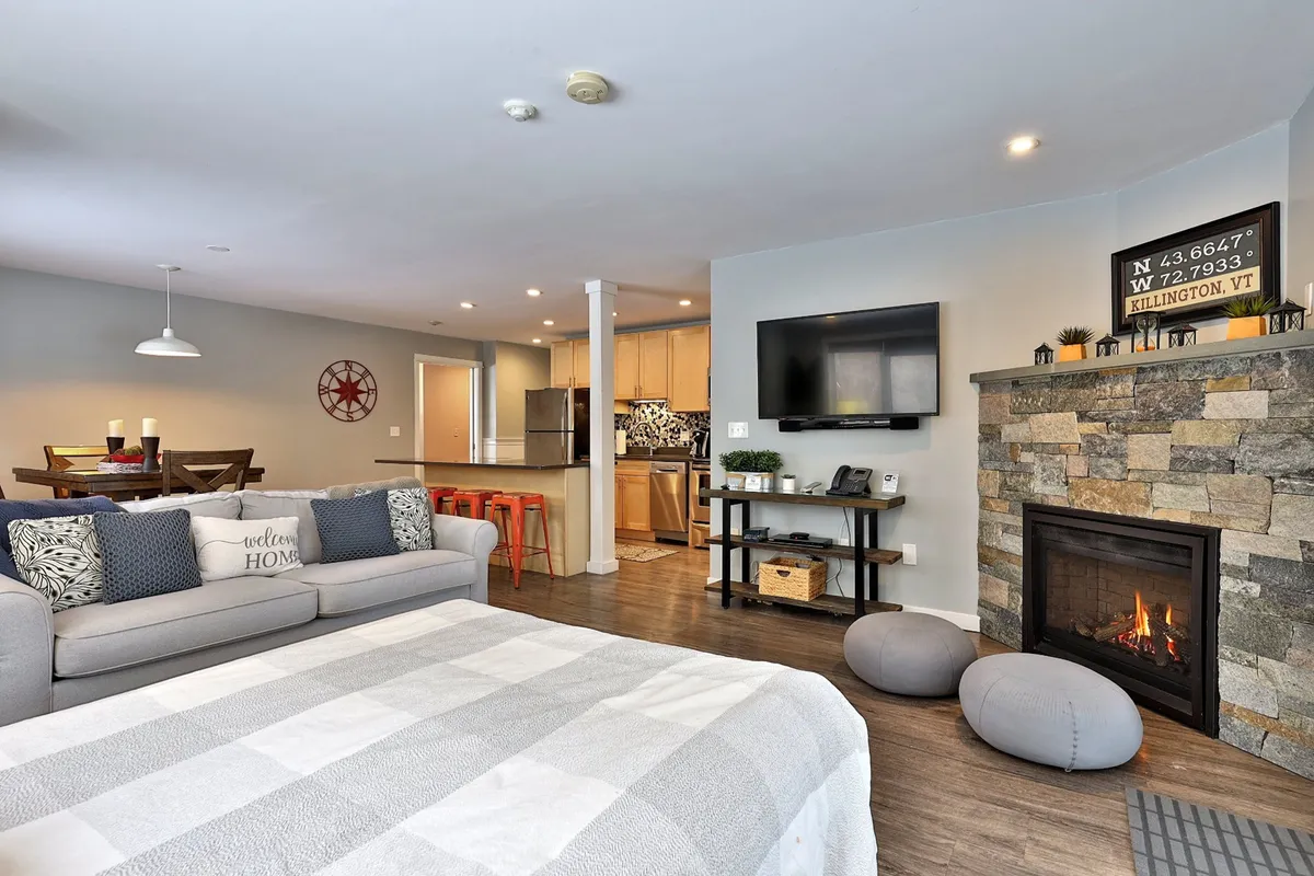 A spacious open-plan living area featuring a cozy fireplace, comfortable sofa, dining table, and an adjacent kitchen area. The space is thoughtfully arranged to promote relaxation, socializing, and family gatherings, with the fireplace as a central comfort feature.