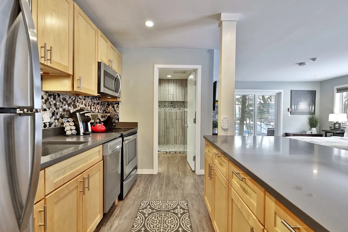 A modern kitchen with stainless steel appliances, wooden cabinets, a spacious kitchen island, and a decorative backsplash. The setting is bright and equipped for cooking, gathering, and entertaining guests, reflecting the suite’s full kitchen amenities.